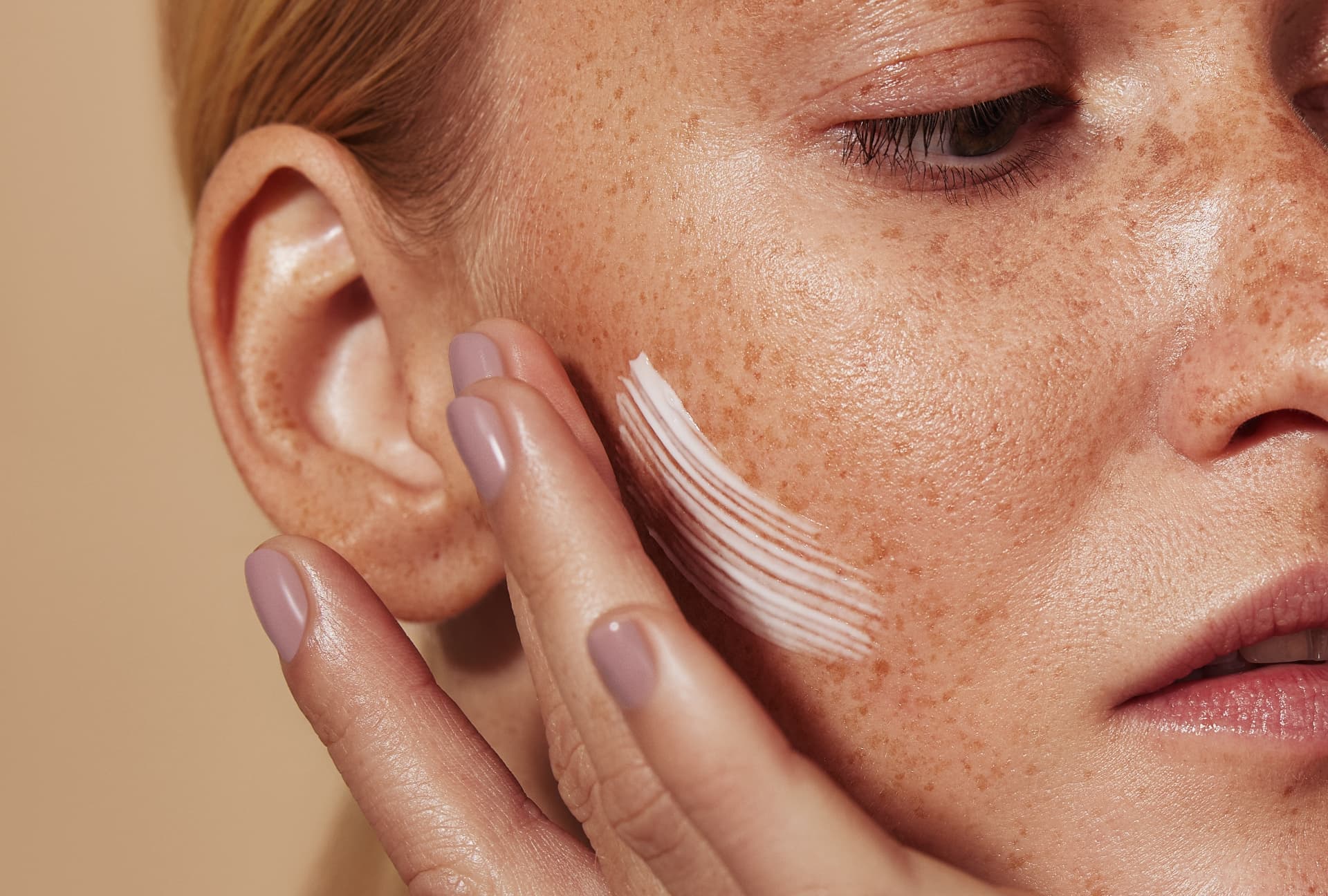Close-up of skin with freckles as cream is smoothed onto the cheek